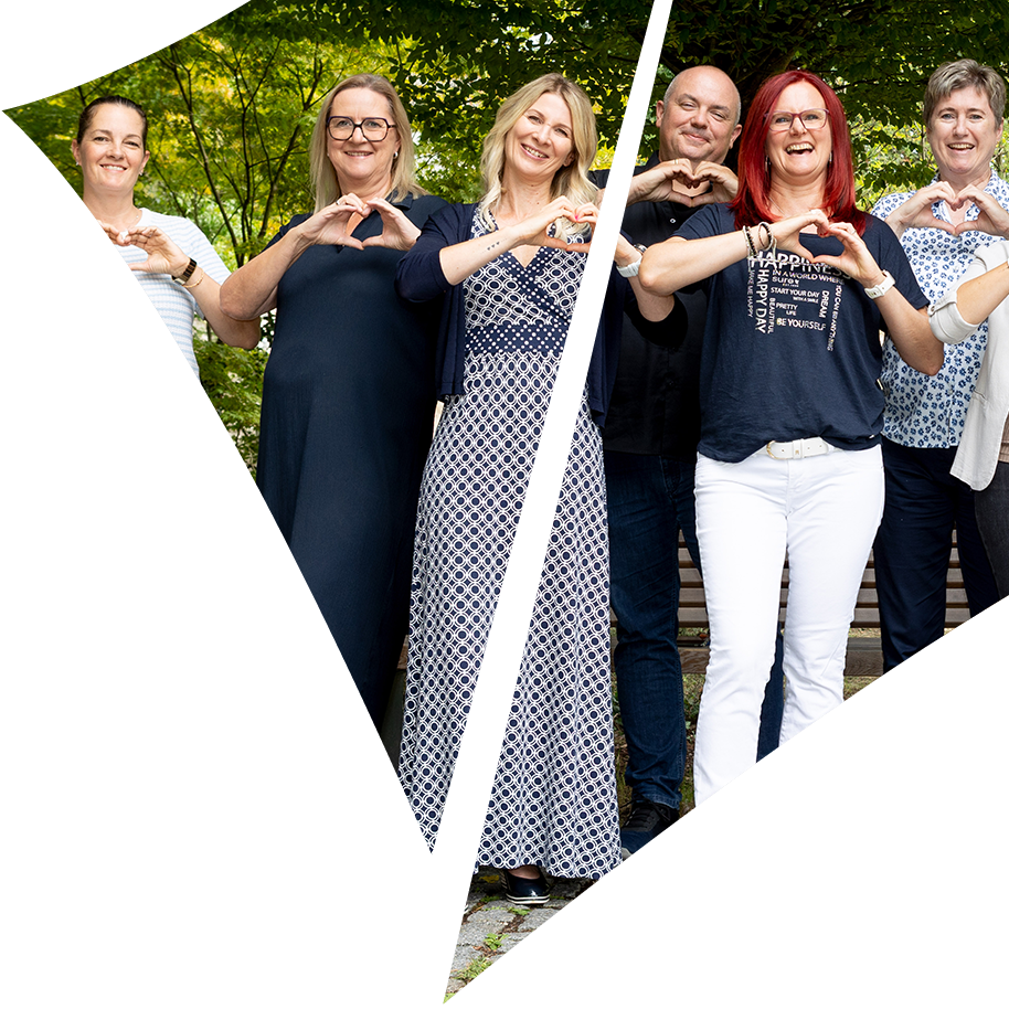 Das lächelnde Ausbildungsteam formt gemeinsam mit den Händen Herz-Gestalten vor einem grünen Hintergrund im Freien, eingebettet in ein dreieckiges grafisches Muster.